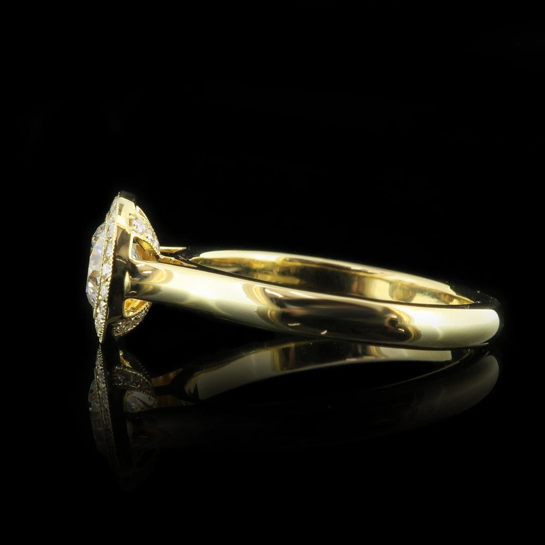 Direct side view of a 2 carat round lab grown diamond halo ring resting on a reflective surface