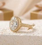 Yellow gold ring with an oversized oval clear gemstone and ornate engraved detailing on the band,