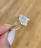 Side angle view of 3 carat oval lab grown diamond ring with pear-cut side stones on rose gold band