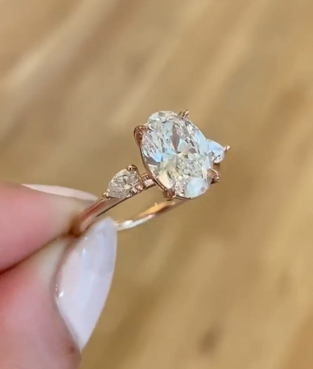 Side angle view of 3 carat oval lab grown diamond ring with pear-cut side stones on rose gold band