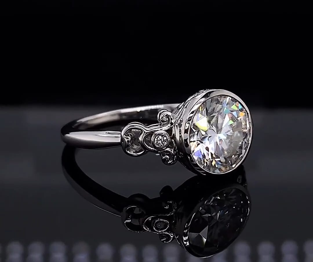 Three-quarter view showing 3 carat round lab diamond in bezel setting with scrollwork side accents
