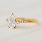 Close-up side profile of a 2 CT pear-cut lab-grown diamond ring in yellow gold showing round accent stones.