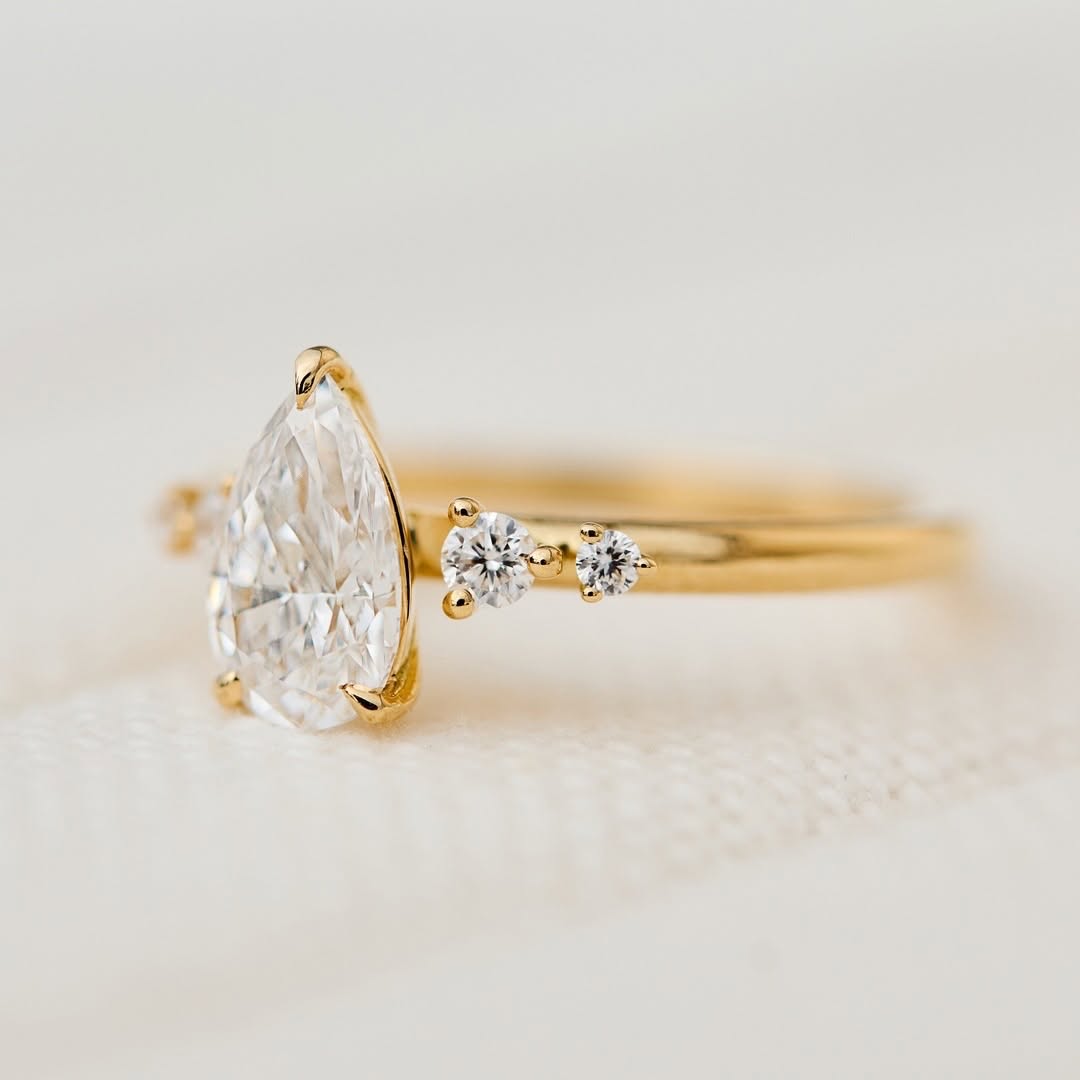 Close-up side profile of a 2 CT pear-cut lab-grown diamond ring in yellow gold showing round accent stones.