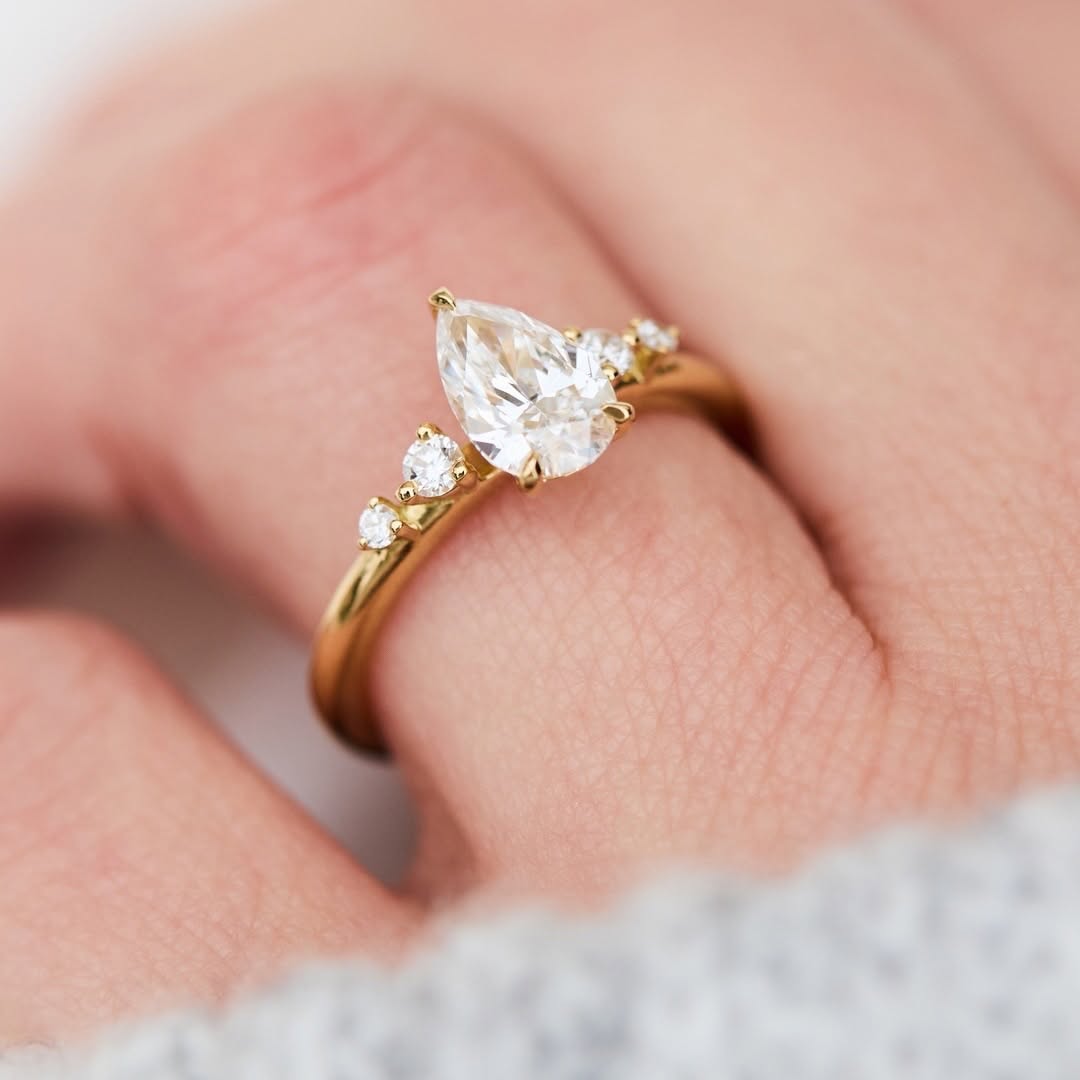 2 carat pear cut lab-grown diamond engagement ring worn on a finger in yellow gold.