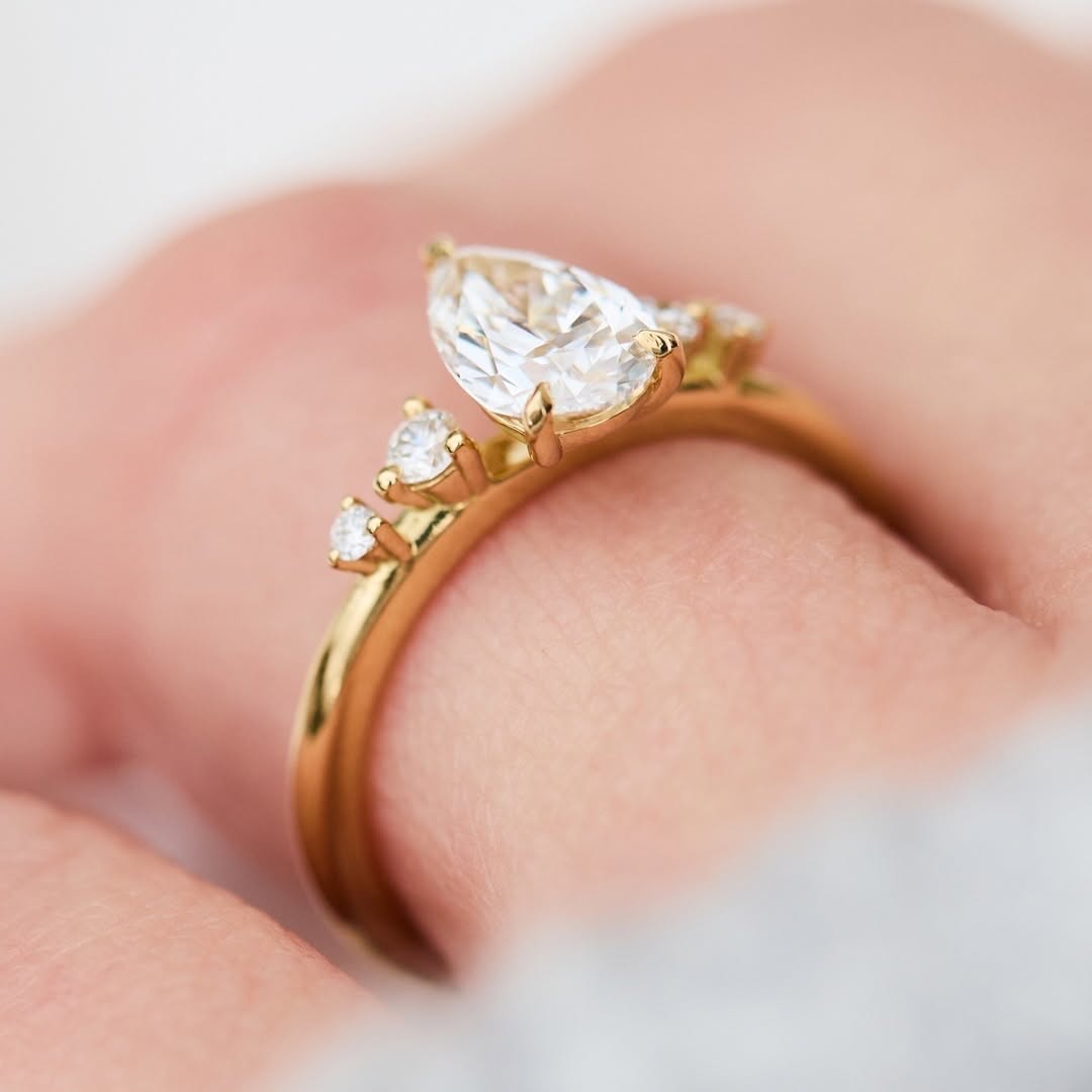 Angle view of a yellow gold pear-shaped lab diamond ring with graduated round side stones on hand.