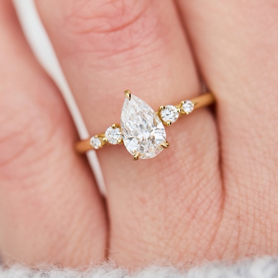 Top-down view of a 2ct pear-shaped lab-created diamond ring with accent diamonds on a finger.