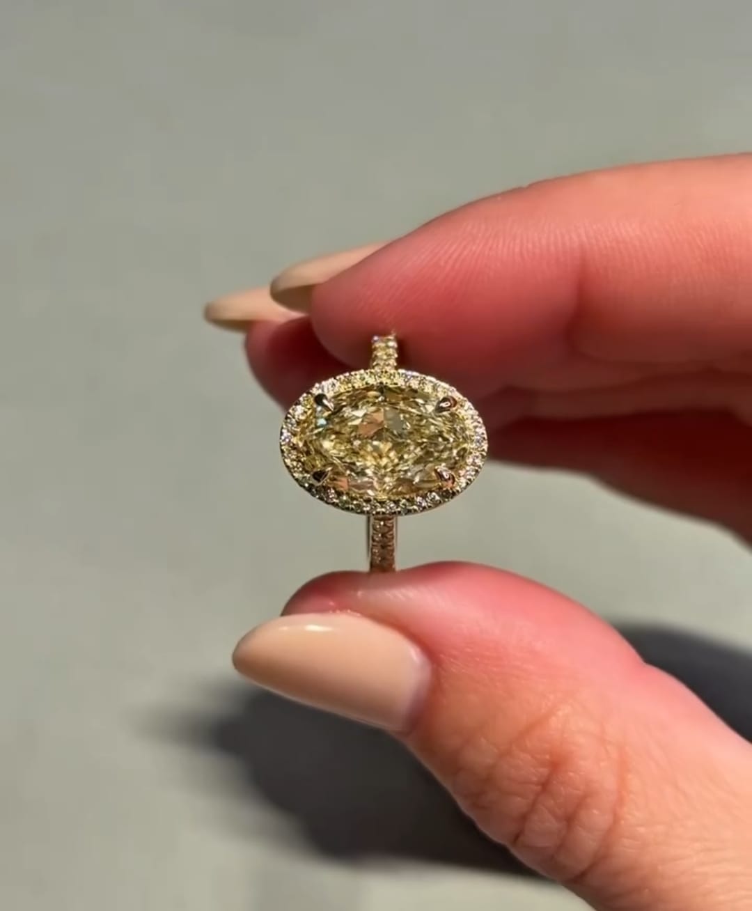 Flat lay view of a 3 carat fancy yellow oval cut lab-grown diamond halo engagement ring on a grey surface.
