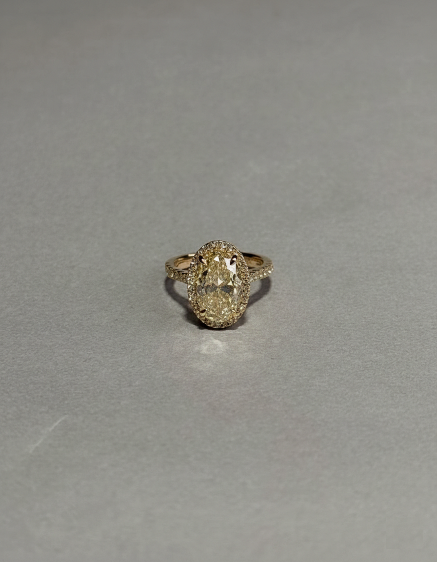 Close-up top view of a 3 CT fancy yellow oval lab-grown diamond ring with a pavé halo held by fingers.