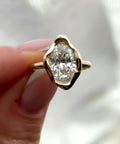 Front view of a 3 CT oval cut lab grown diamond ring held in fingers showing the wavy yellow gold bezel setting.