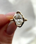 Front view of a 3 CT oval cut lab grown diamond ring held in fingers showing the wavy yellow gold bezel setting.