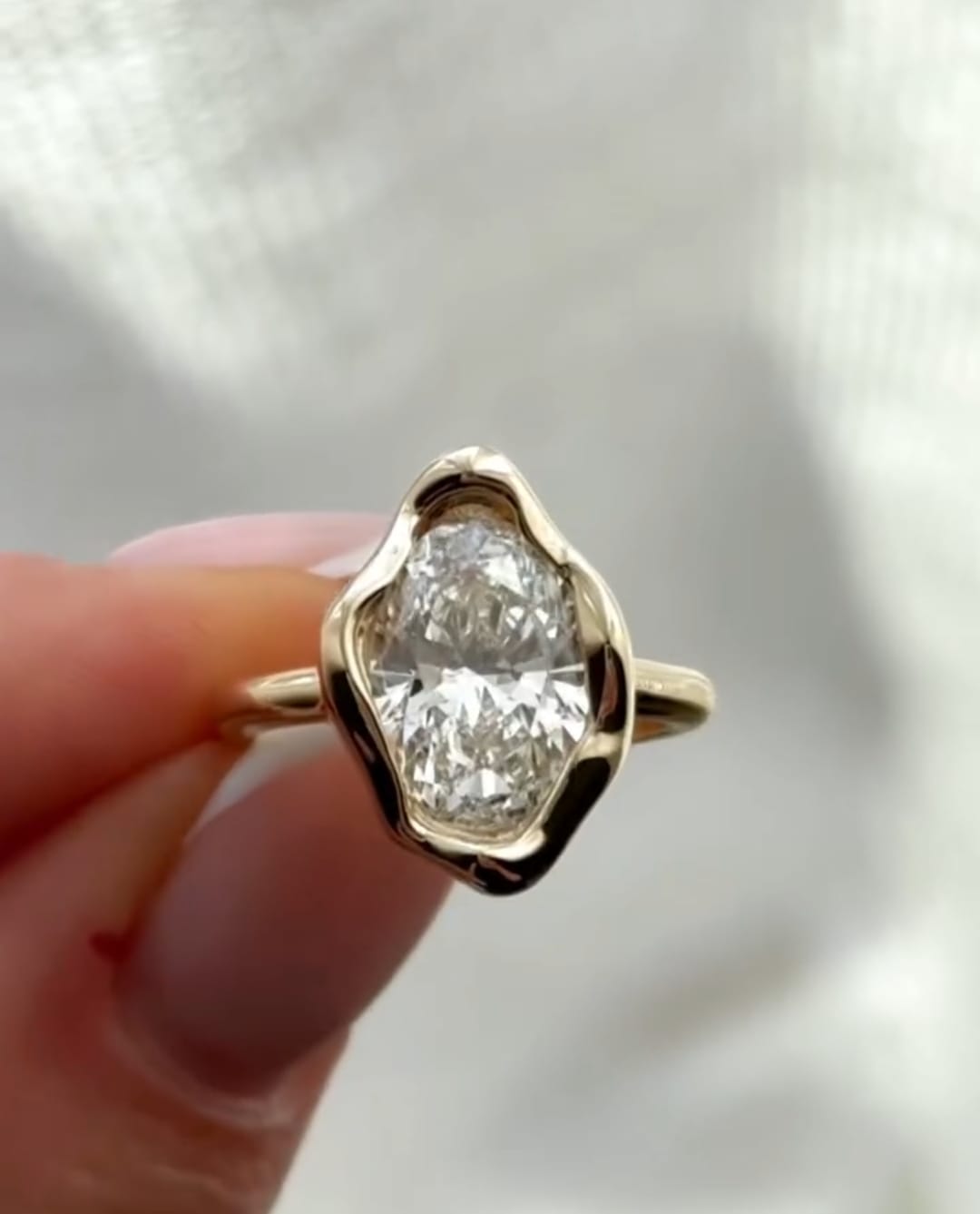 Underneath side profile showing the raised setting and band of an organic oval bezel diamond ring.