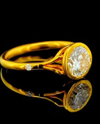 Side profile view of a 2 CT round lab grown diamond bezel set engagement ring in yellow gold showing side accent diamond