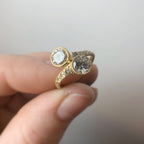 Hand holding a two-stone round cut lab grown diamond Toi et Moi bypass ring in yellow gold with milgrain bezel settings