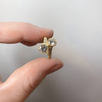 Direct view of a romantic two stone round lab grown diamond bypass ring with milgrain detailing held in hand