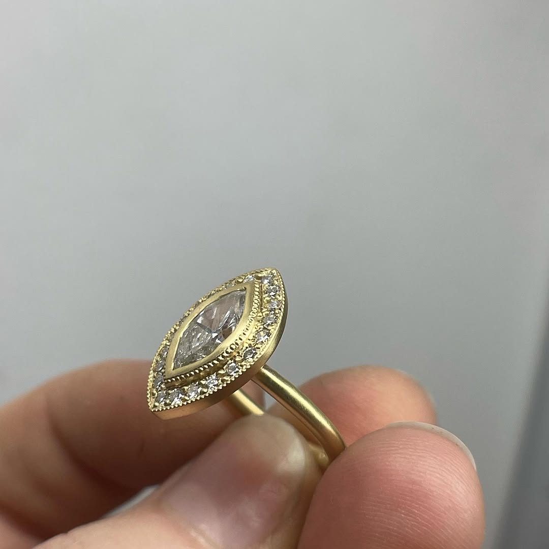 Side angle view showing the thin matte yellow gold band and bezel setting of the marquise diamond ring