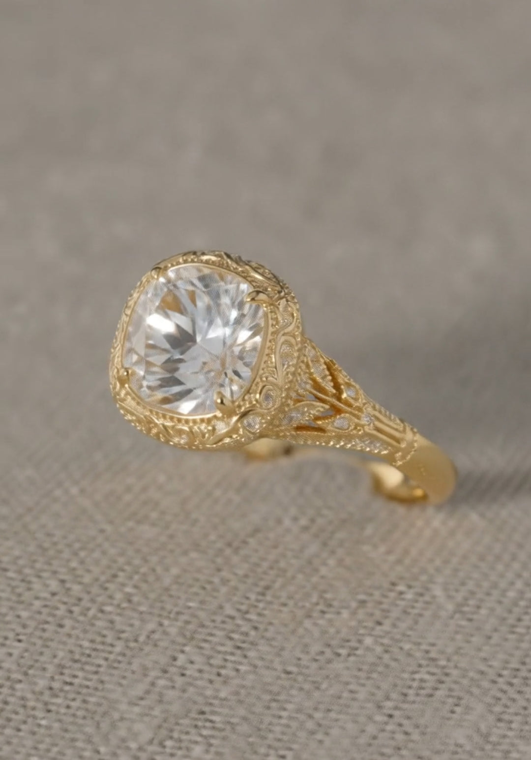 Angled view of an ornate yellow gold engagement ring featuring a large brilliant center stone and detailed antique-style engraving on the band.