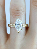 Top view of a 3 carat marquise cut lab grown diamond engagement ring with a vintage engraved yellow gold band worn on a finger