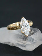 3 carat marquise lab diamond engagement ring with an intricately engraved yellow gold band resting on a quartz crystal