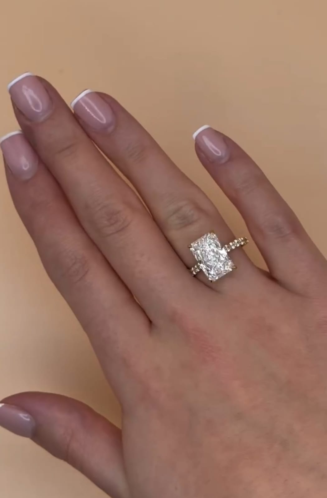 Top-down view of a 3 carat elongated radiant cut lab grown diamond engagement ring worn on a woman's hand.