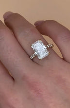 Angled view of an elongated radiant cut lab grown diamond ring with a diamond pavé band worn on a finger.