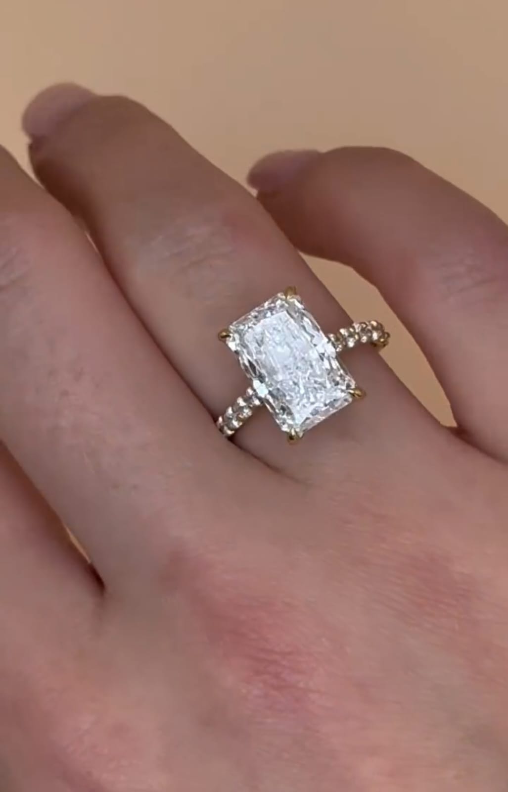 Angled view of an elongated radiant cut lab grown diamond ring with a diamond pavé band worn on a finger.