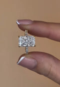 Close up front view of a 3 carat radiant cut lab diamond engagement ring held between two fingers, highlighting its brilliant facets.