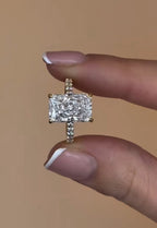 Close up front view of a 3 carat radiant cut lab diamond engagement ring held between two fingers, highlighting its brilliant facets.