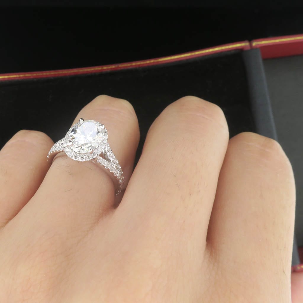 Close-up angled view of a 2 carat oval diamond halo engagement ring being worn on a hand.
