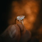 Close-up of a brilliant pear cut lab grown diamond set in a rustic gold twig band, held delicately between fingers.