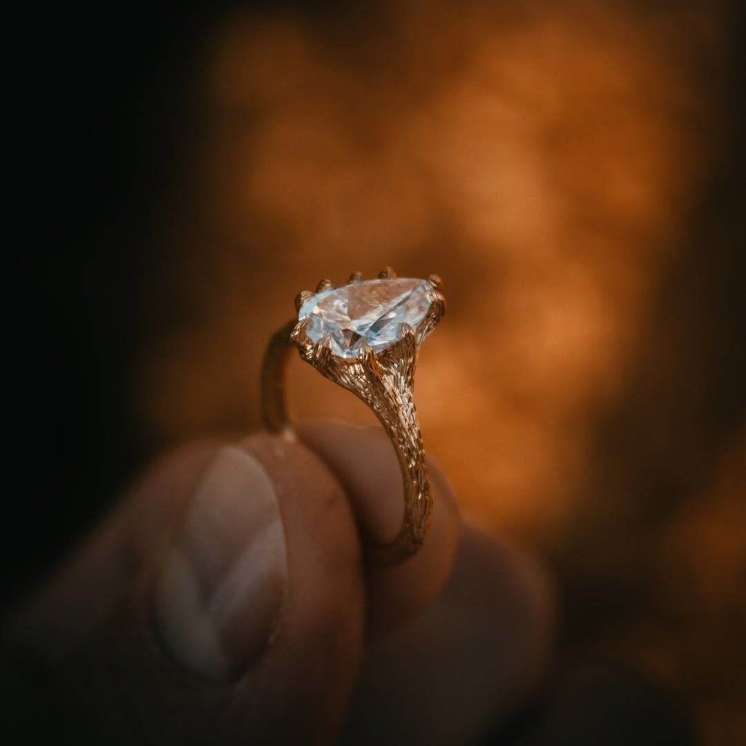 Close-up of a brilliant pear cut lab grown diamond set in a rustic gold twig band, held delicately between fingers.