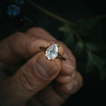 Top-down view of a 2 CT pear shaped diamond ring with a tree bark textured gold band against a dark natural background.