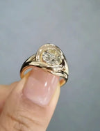 Front-angled view of a modern 2 carat round cut lab grown diamond ring, featuring a sleek gold swirl bypass setting, held delicately between fingers.