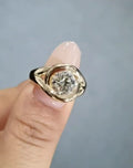Top-down view of a brilliant 2 CT round lab grown diamond engagement ring showing the fluid, wrap-around gold metalwork resting on a finger.