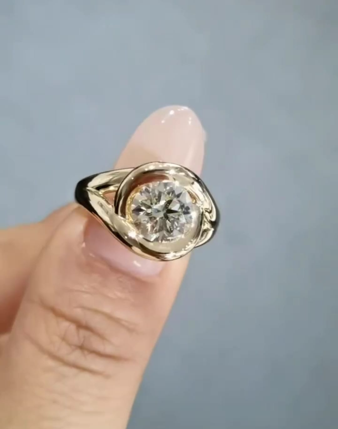 Top-down view of a brilliant 2 CT round lab grown diamond engagement ring showing the fluid, wrap-around gold metalwork resting on a finger.