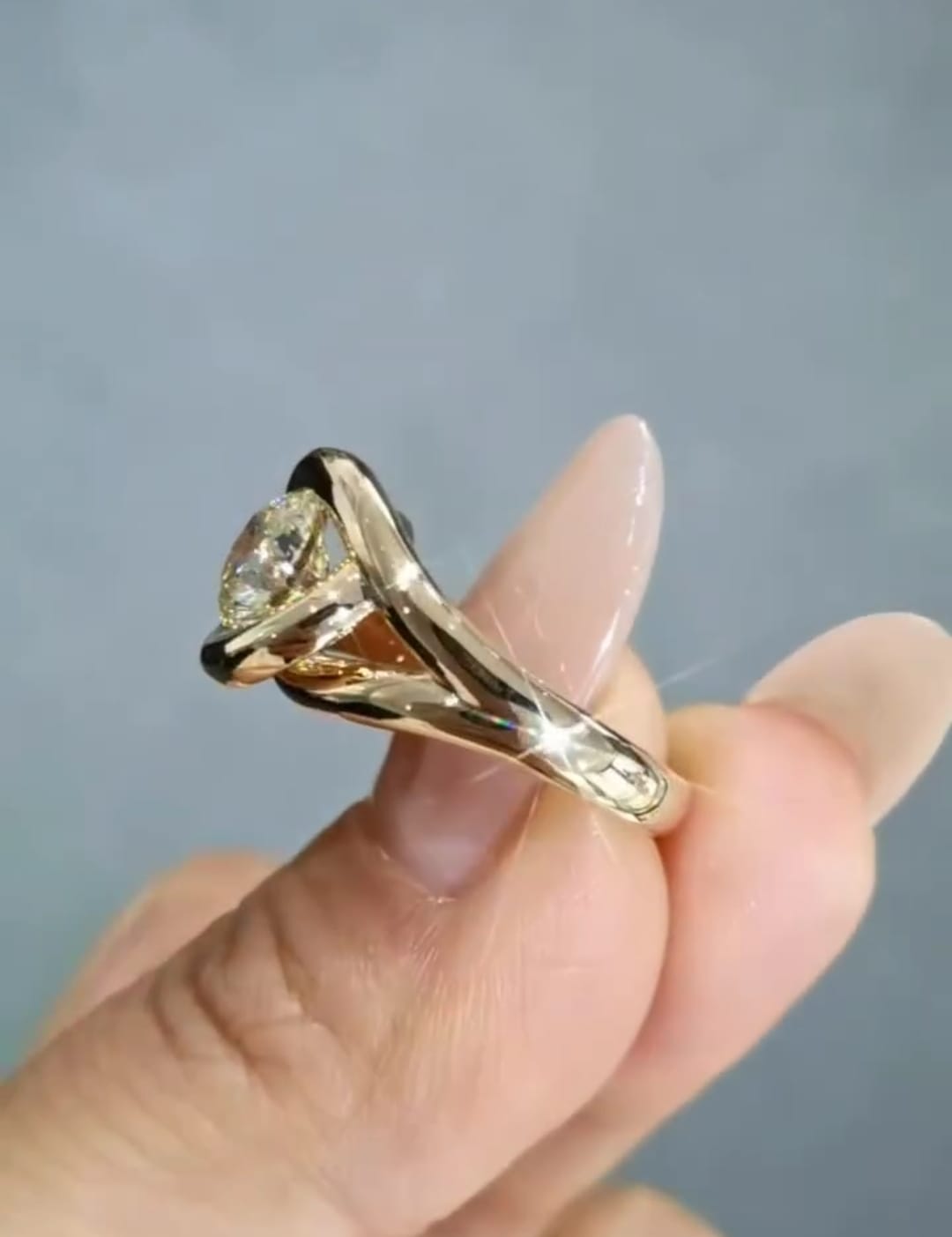 Side profile of a sculptural yellow gold engagement ring, highlighting the smooth bypass setting that secures a 2 carat round lab created diamond.