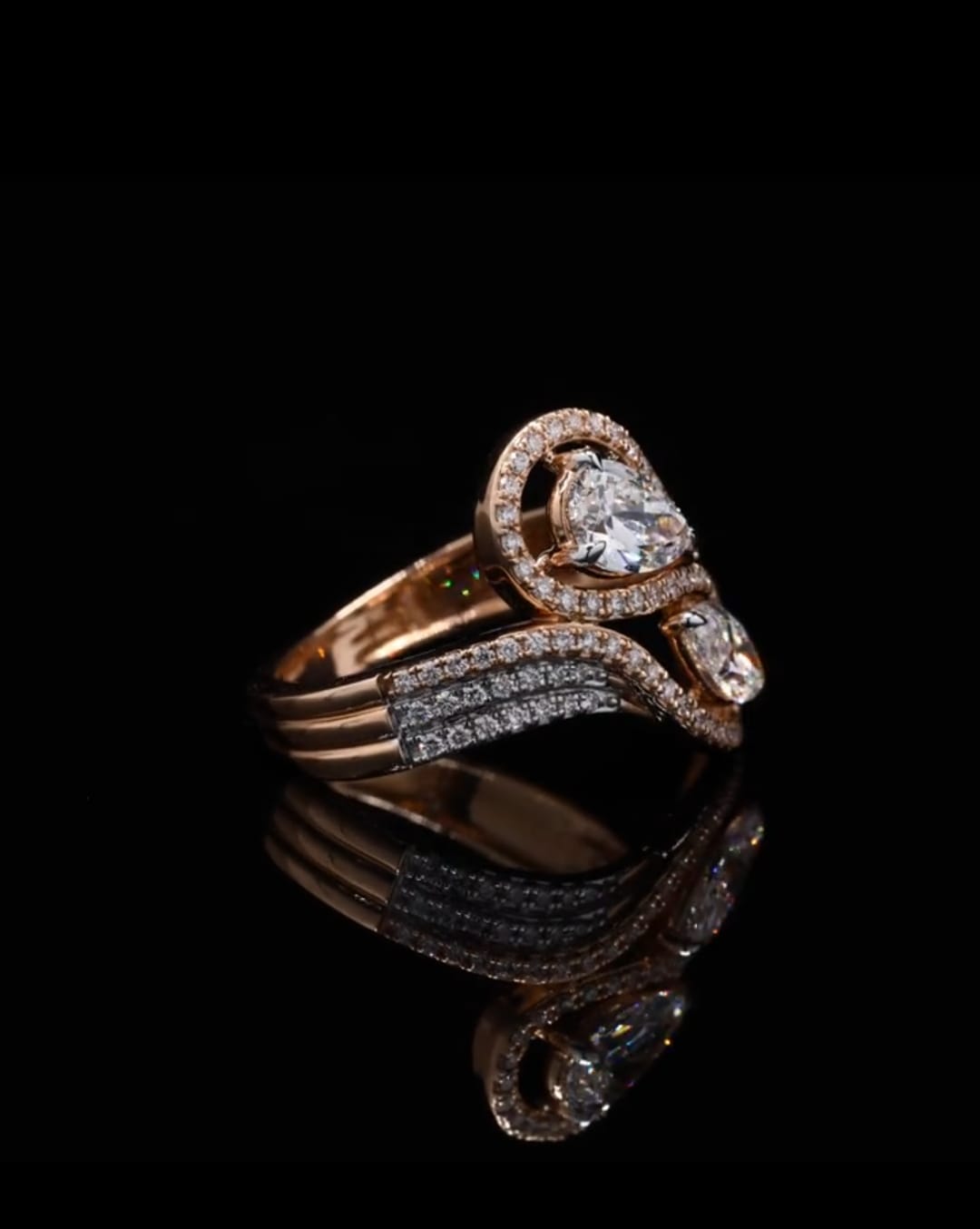 Angled side view of a Pear and Marquise cut lab grown diamond bypass ring with diamond halos, beautifully reflected on a black surface.