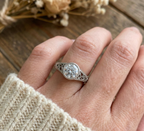 Angled side profile of a silver filigree engagement ring showcasing the intricate scrollwork along the band and under the bezel setting.