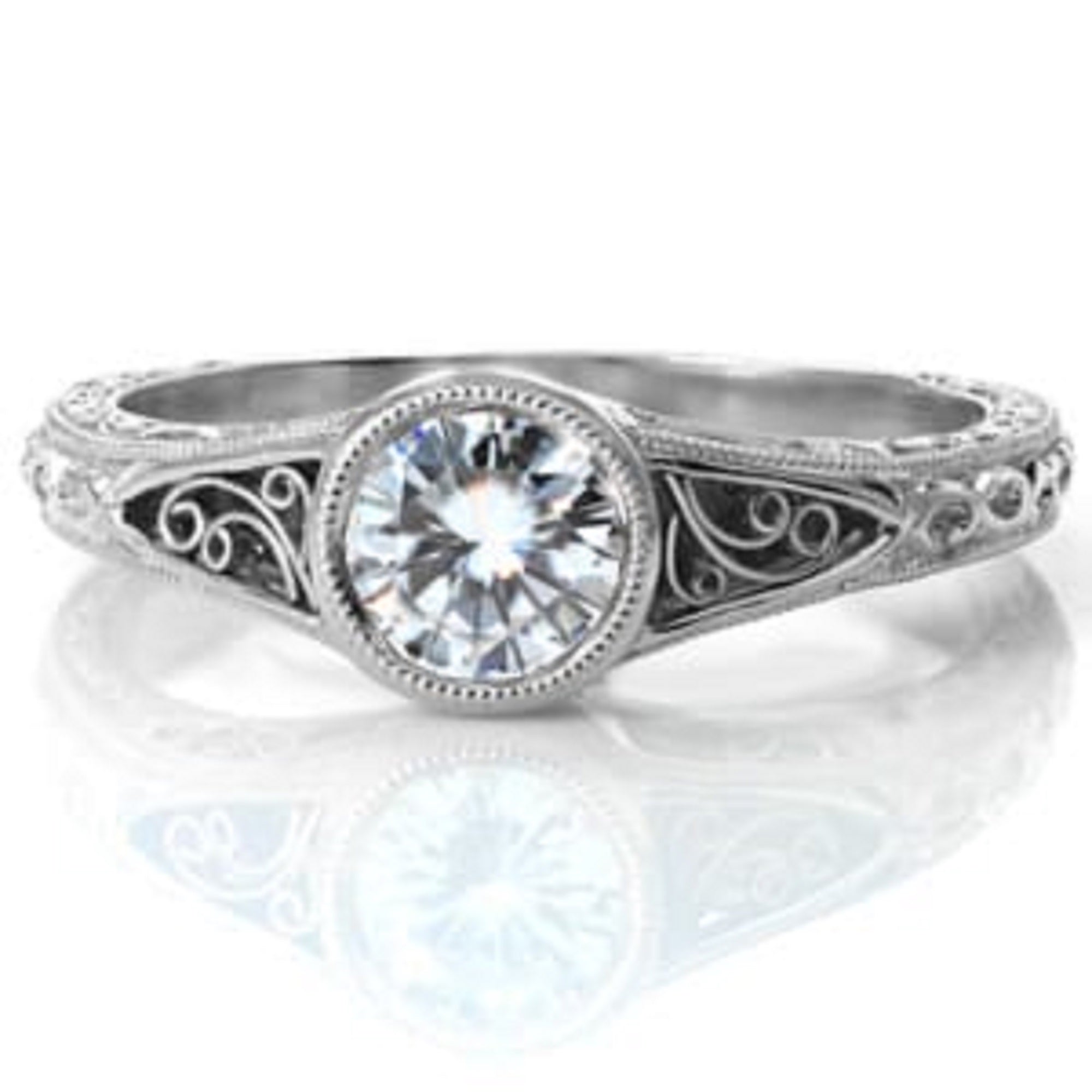Straight front-facing view of a vintage round cut engagement ring with an intricate filigree band reflecting on a white surface.