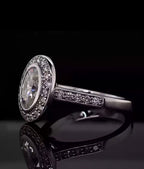 Side-angle view of a 3 carat oval lab diamond ring featuring a bezel set halo and pavé band on a dark reflective background.