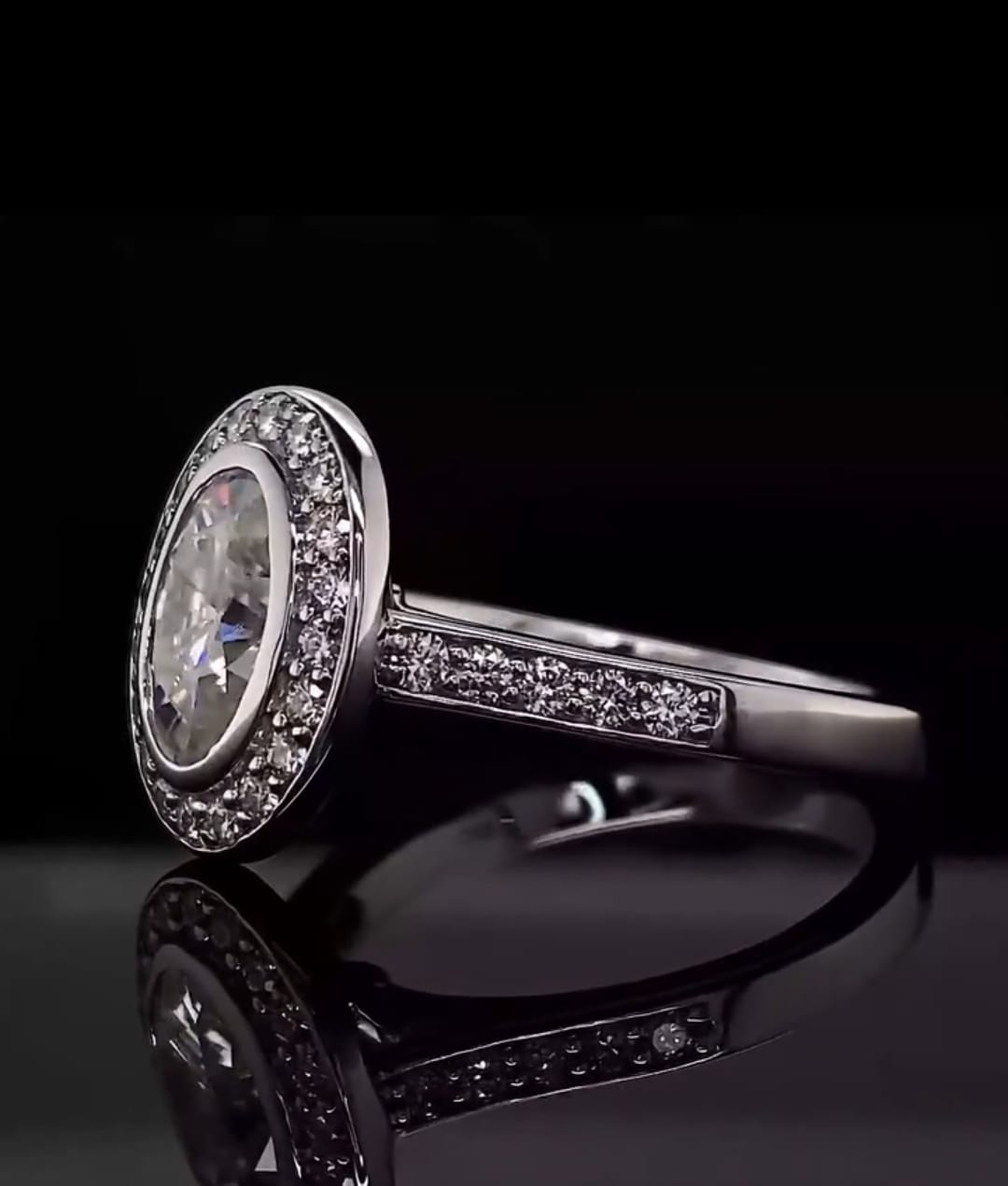 Side-angle view of a 3 carat oval lab diamond ring featuring a bezel set halo and pavé band on a dark reflective background.
