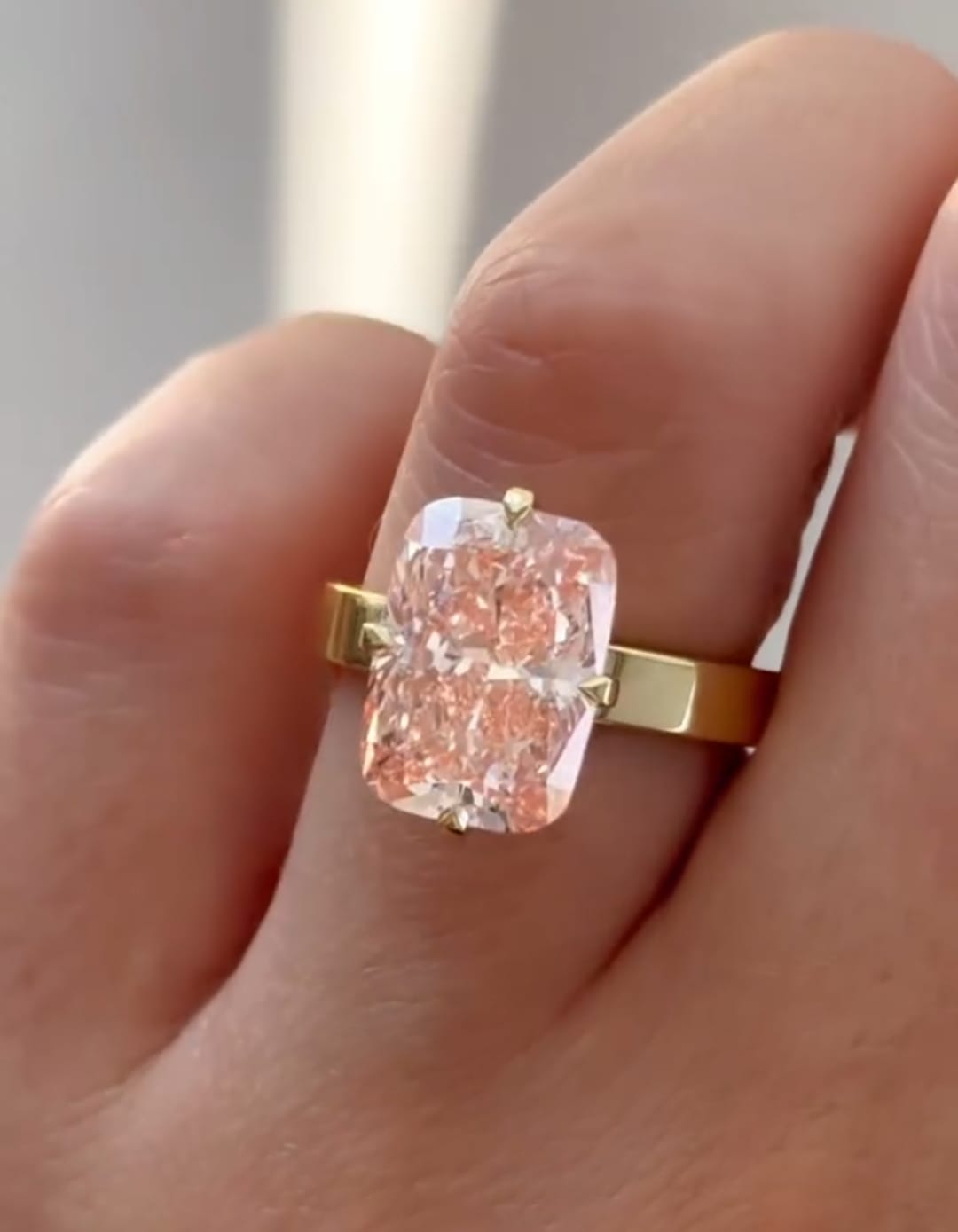 Top-down view of a stunning 3 ct pink elongated radiant cut lab diamond solitaire ring worn on a finger.