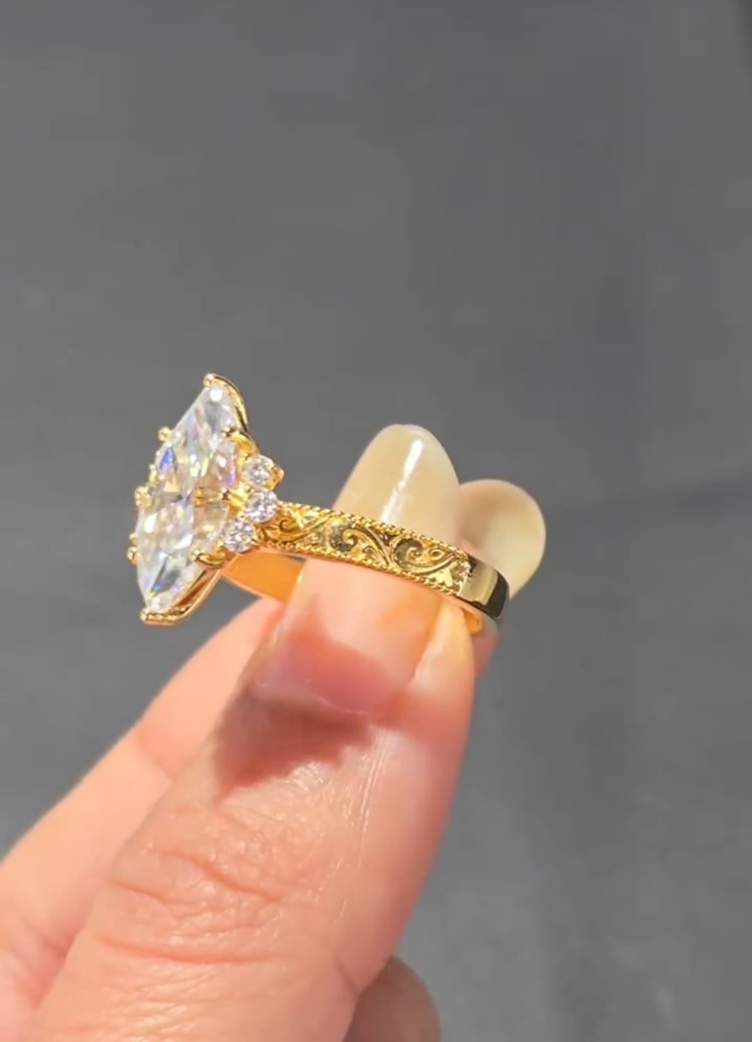 Angled view of a marquise cut lab created diamond ring displaying detailed gold band engraving and brilliant side stones.
