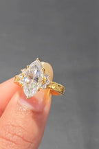 Hand holding a sparkling 3 carat marquise diamond ring catching the light, showcasing its brilliance and gold filigree details.