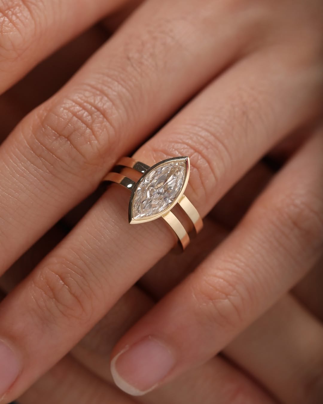 Top-down view of a woman's hand wearing a modern lab grown diamond ring with a gold double band design.