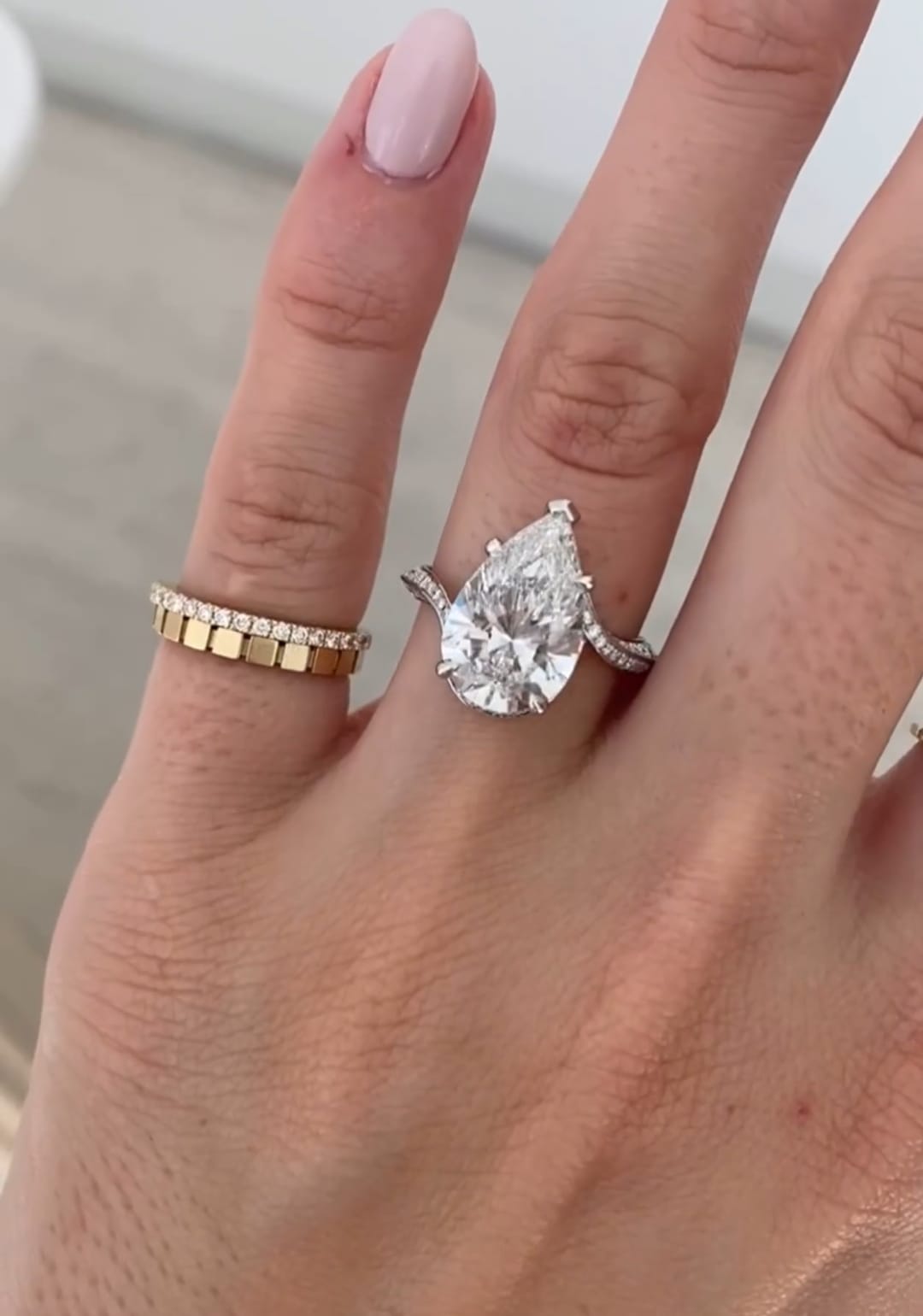 Woman wearing a large 4 carat pear cut lab grown diamond engagement ring on her hand alongside a gold band.
