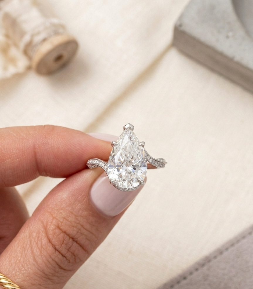 Close up of a beautifully faceted 4 CT pear lab grown diamond ring held between fingers.