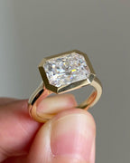 Close-up of a 3 carat radiant cut lab grown diamond in a horizontally set yellow gold bezel ring.