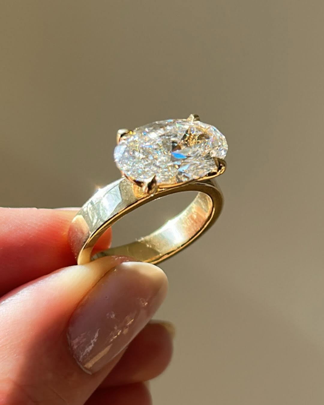 Hand holding 2 carat East-West set oval lab grown diamond ring in 18K yellow gold