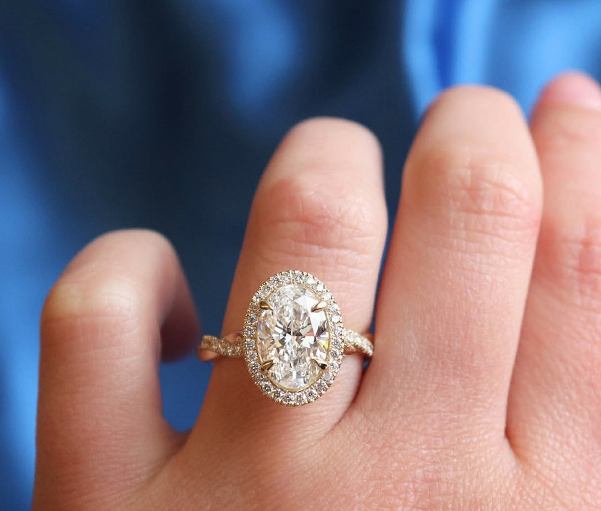 Close-up top-down view of 3 CT oval lab diamond ring with sparkling halo setting on finger.