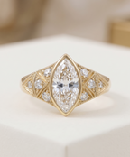 Top-down view of a vintage-inspired yellow gold engagement ring featuring a bezel-set marquise center stone and geometric milgrain side panels.